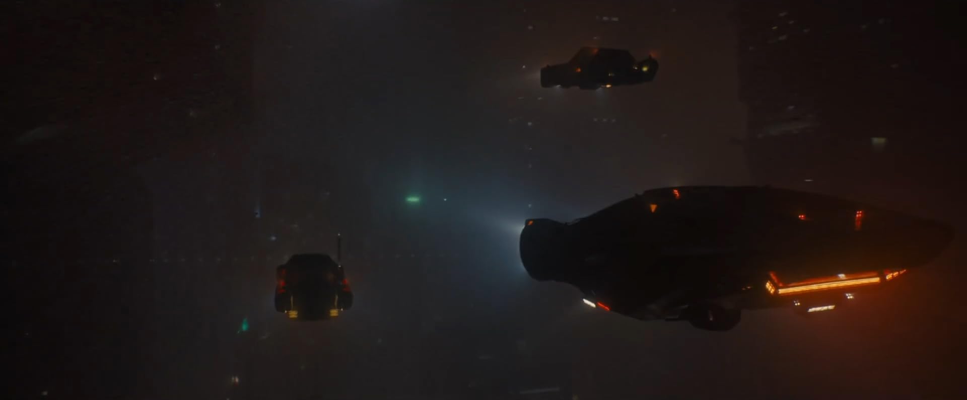 Scene from the film showing three car like vehicles flying through a foggy, polluted, nighttime city.
